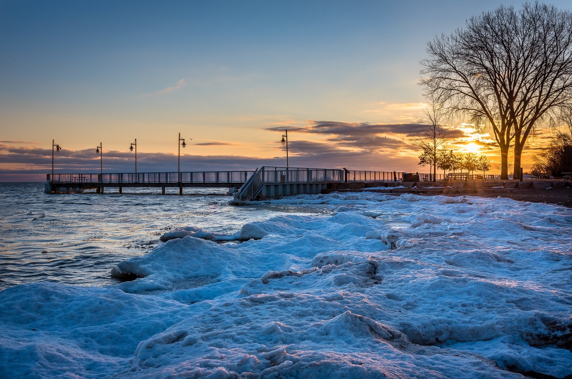4K Ultra HD photo of an icy shoreline and wooden pier at sunset in Ontario, Canada, showcasing ocean waves and a serene winter landscape.