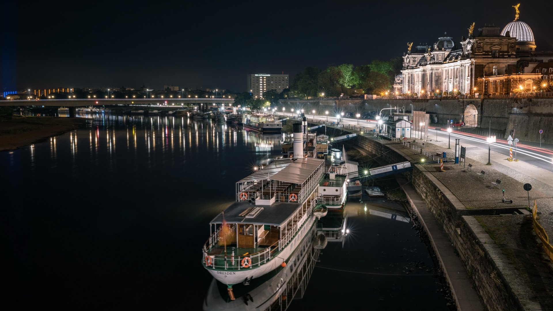 4K Ultra HD PC desktop wallpaper: Dresden night scene of man-made riverfront with illuminated historic buildings, bridges and docked riverboats reflected on calm water.