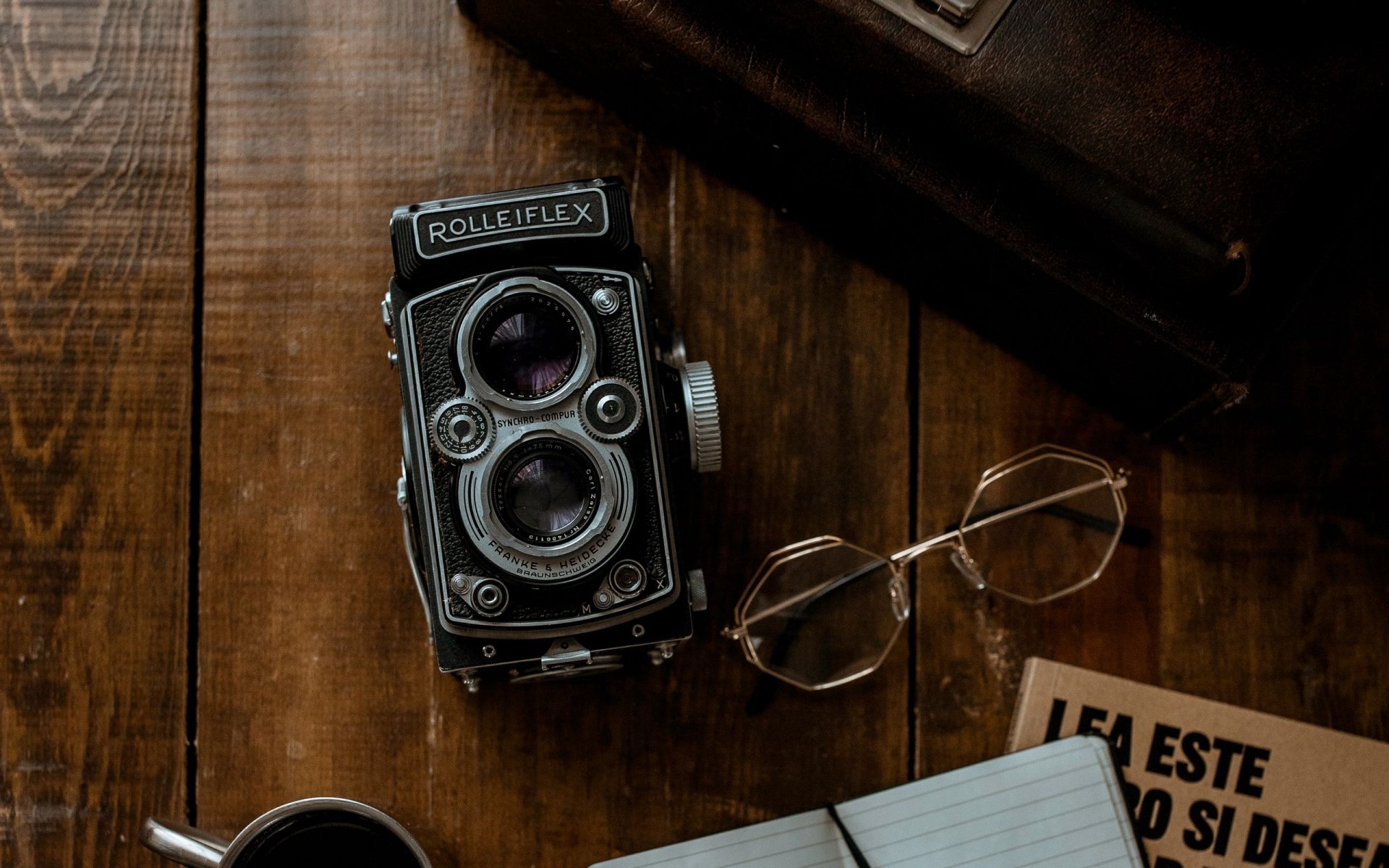 Vintage Rolleiflex camera, eyeglasses, and an open book arranged on a wooden surface, creating a nostalgic photography-themed HD desktop wallpaper background.