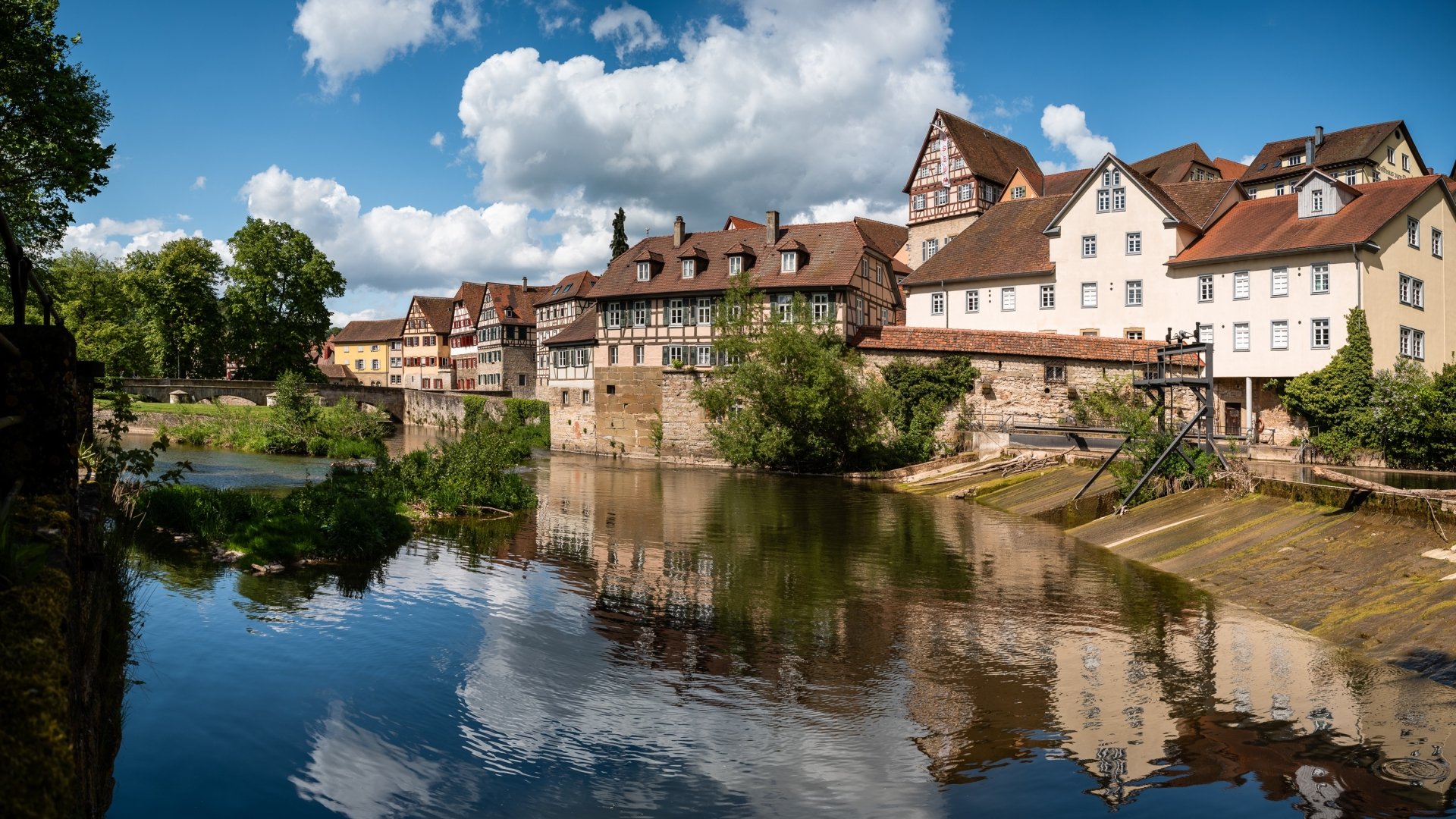 Scenic view of traditional houses along a river in Baden-Württemberg, Germany, with reflections and clouds in the water, captured as an HD desktop wallpaper background.