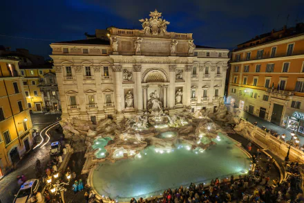 Night view of the illuminated Trevi Fountain in Rome, Italy, showcasing its intricate man-made sculptures and surrounding architecture in a high-definition desktop wallpaper.