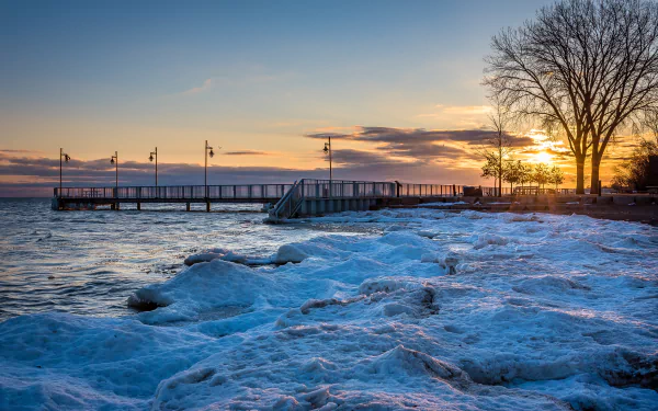 4K Ultra HD photo of an icy shoreline and wooden pier at sunset in Ontario, Canada, showcasing ocean waves and a serene winter landscape.