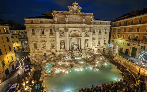 Night view of the illuminated Trevi Fountain in Rome, Italy, showcasing its intricate man-made sculptures and surrounding architecture in a high-definition desktop wallpaper.