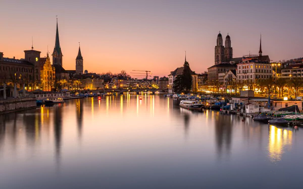 4K Ultra HD view of Zurich, Switzerland at dusk, showcasing the calm river, illuminated man-made bridge, and historic city skyline.