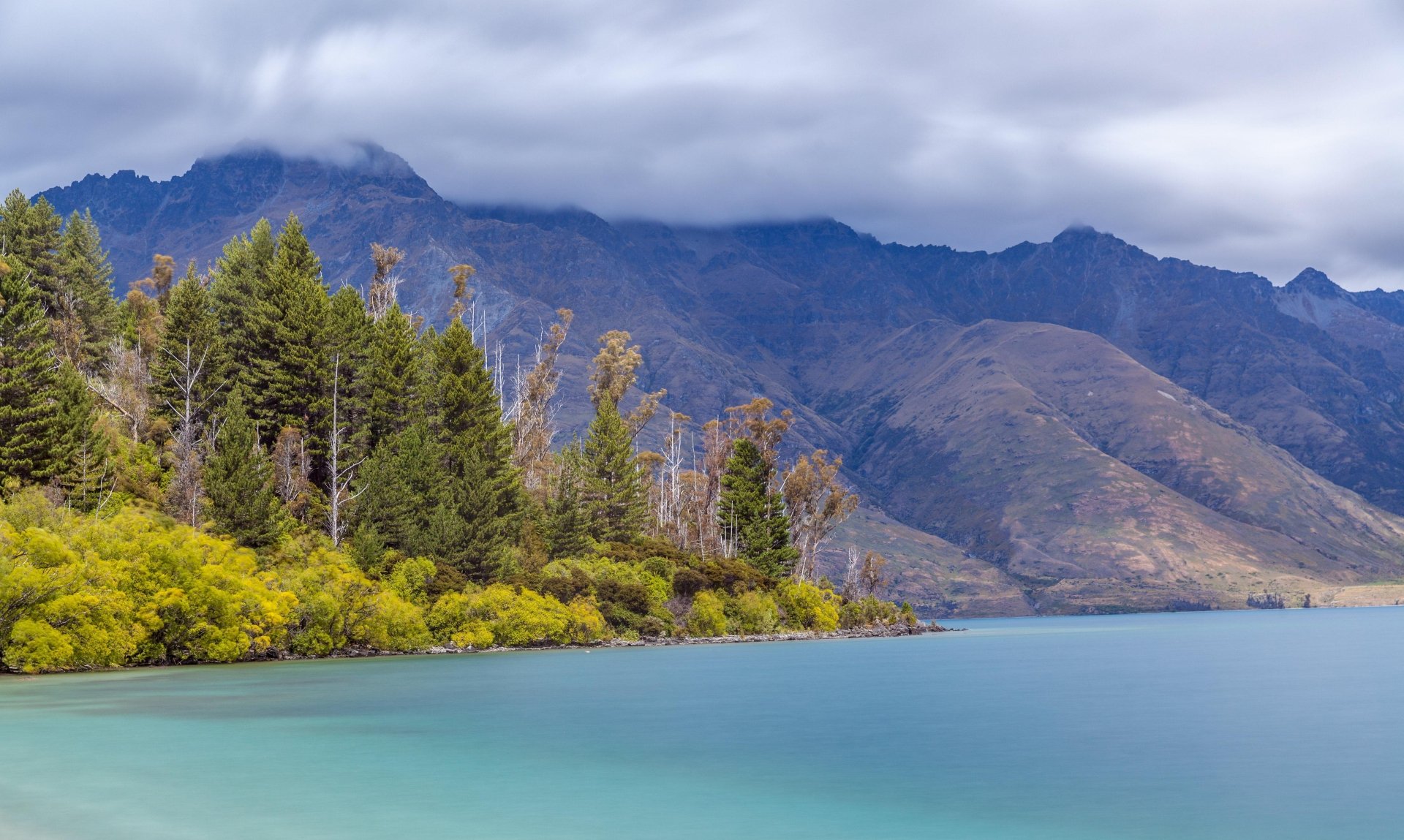 4K Ultra HD desktop wallpaper depicting a serene lake bordered by lush forest with mountains in the background under a cloudy sky.