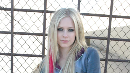 4K Ultra HD PC desktop wallpaper: blonde pop-punk musician with a pink hair streak and smoky eye makeup standing by a chain-link fence, music-themed portrait.