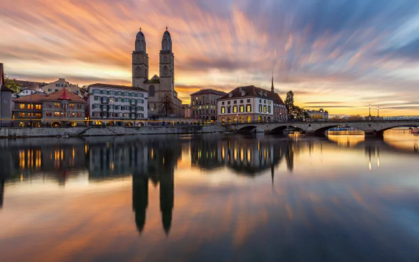 4K Ultra HD image of Zurich's skyline at sunset, featuring historic buildings and a calm river reflecting the vibrant sky, highlighting man-made architecture.