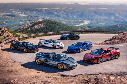 A lineup of six McLaren 600LT supercars in various colors, parked on a mountain road with a scenic mountain landscape in the background, rendered in 4K Ultra HD.