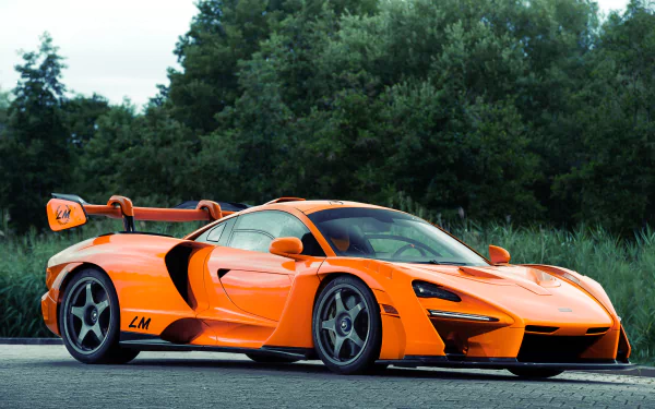 Orange McLaren Senna GTR supercar parked on a road with a forest backdrop — high-detail 4K Ultra HD PC desktop wallpaper/background.