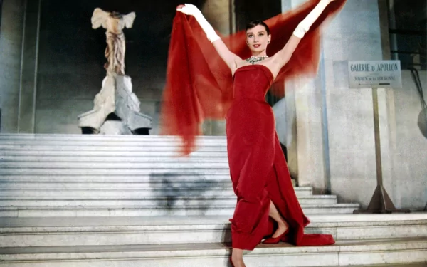 HD desktop wallpaper featuring Audrey Hepburn in an elegant red dress, striking a graceful pose on grand steps with dramatic lighting.