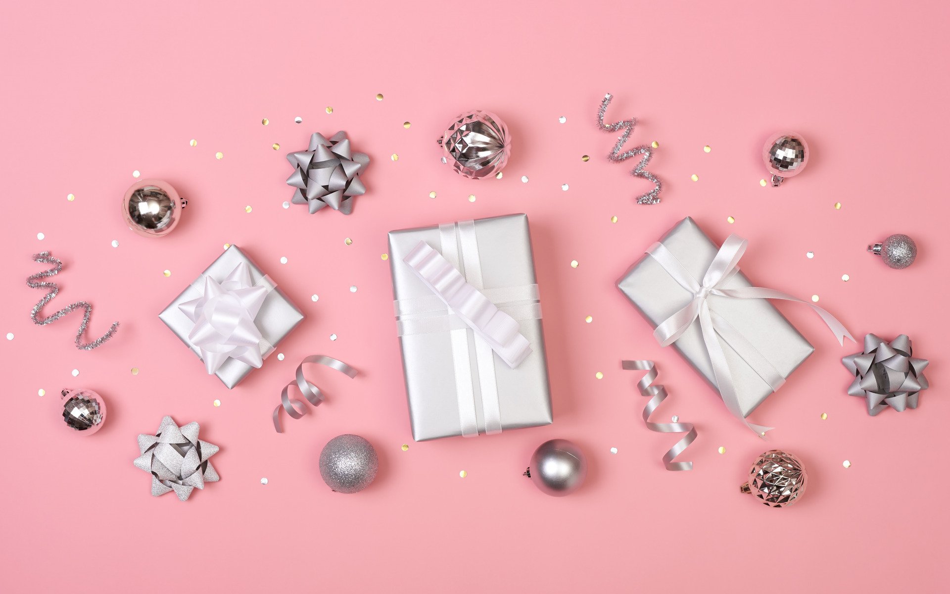 HD desktop wallpaper featuring a holiday scene with silver Christmas ornaments, gift boxes wrapped in white and silver, set against a soft pink background.