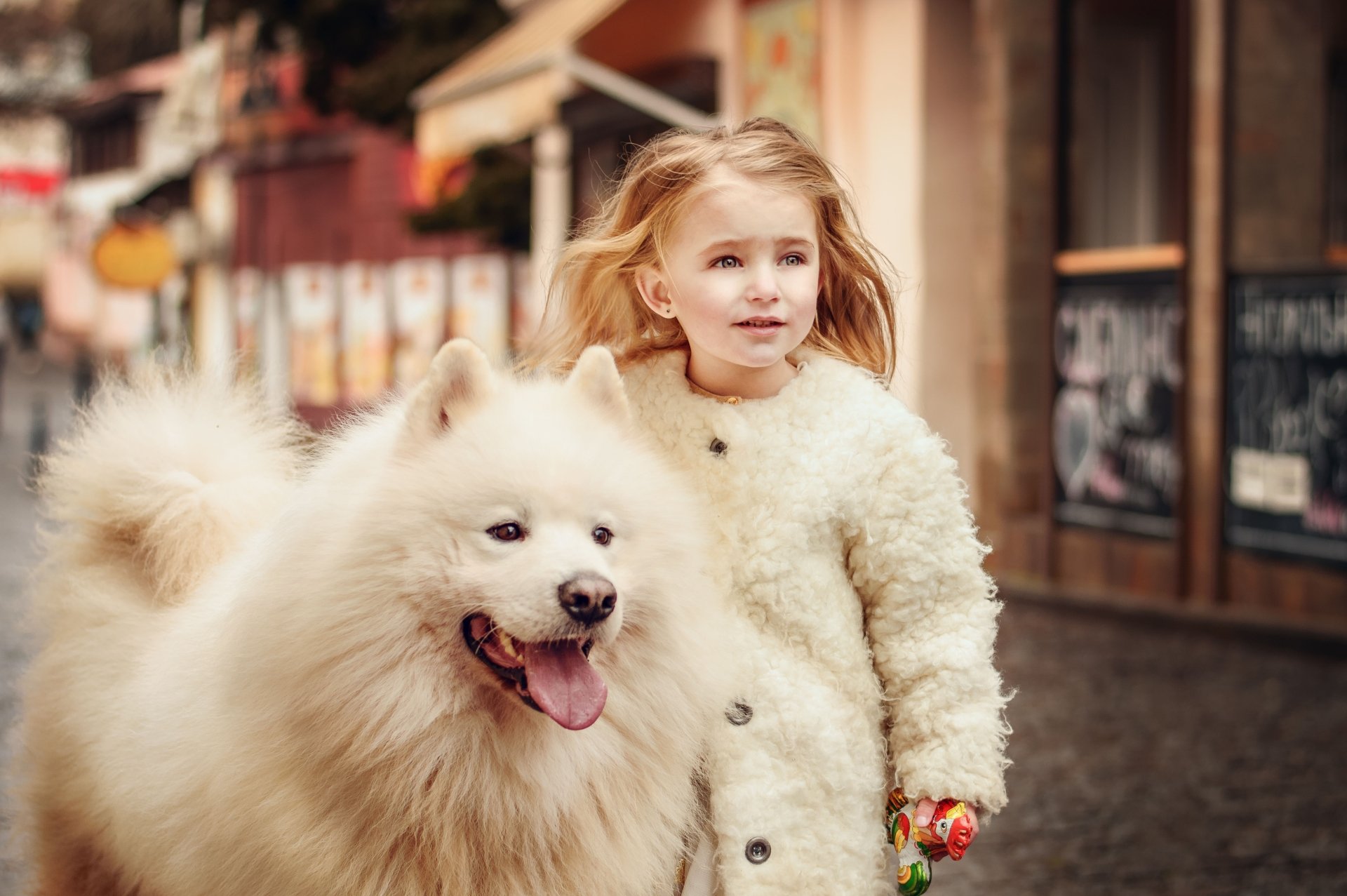 5K Ultra HD PC desktop wallpaper: joyful mood photography of a child in a white coat walking a fluffy Samoyed dog down a city street.