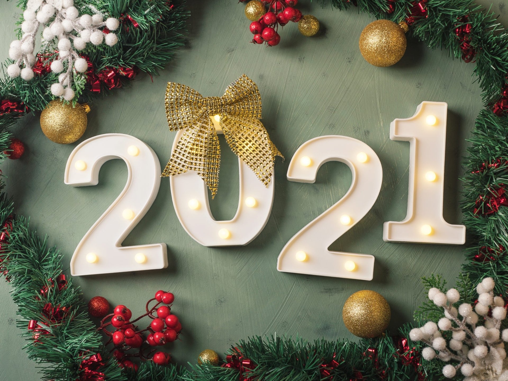 Holiday New Year 2021 HD PC desktop wallpaper and background — lit 2021 numerals with a gold bow, evergreen garland, red berries and gold ornaments on a green backdrop.