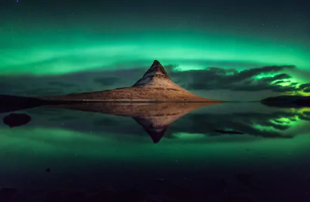 Aurora borealis lights up the night sky over Kirkjufell mountain in Iceland, beautifully reflected in the calm water under a starry sky.