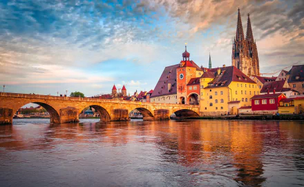 Historic bridge spanning the Danube River in Regensburg, Bavaria, Germany, with cityscape and cathedral under a vibrant sky, captured in HD for desktop wallpaper.