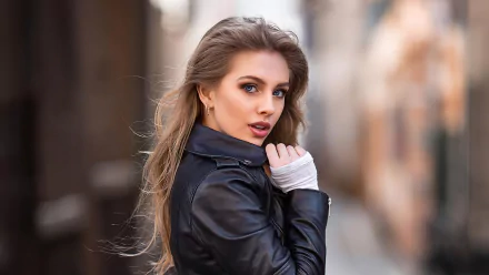 Close-up of a makeup-wearing female model in a black jacket, over-the-shoulder pose against a blurred street — 2K Quad HD PC desktop wallpaper background.