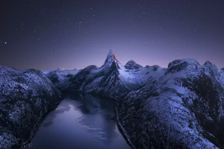Snow-covered Norwegian mountain peaks under a starry winter night sky, reflected in a calm pond, captured in a high-definition desktop wallpaper.