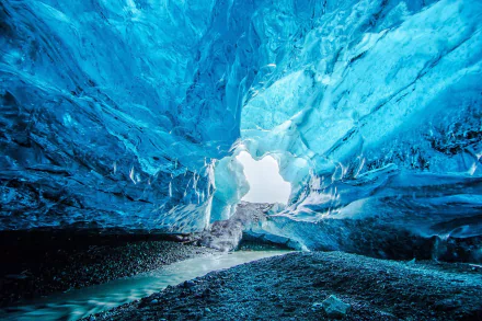 Ice cave inside Vatnajökull glacier in Iceland’s Vatnajökull National Park, showcasing vibrant blue ice formations and rocky ground, captured as an HD desktop wallpaper.