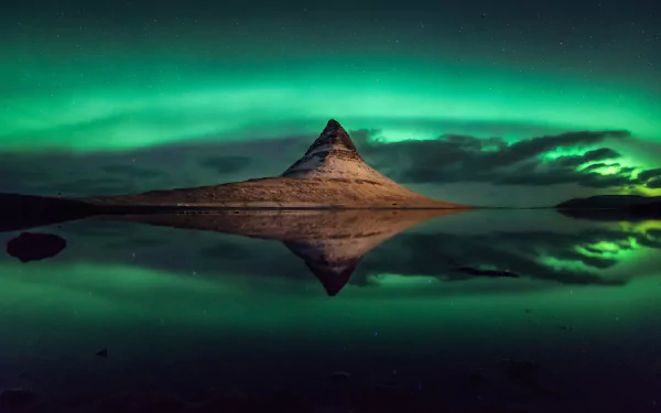 Aurora borealis lights up the night sky over Kirkjufell mountain in Iceland, beautifully reflected in the calm water under a starry sky.