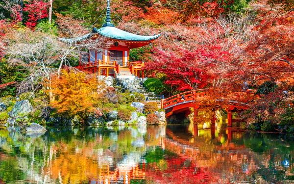 A serene autumn scene at Daigo-ji temple in Kyoto, Japan, featuring vibrant fall foliage, a red bridge, and traditional architecture reflected in a calm lake.