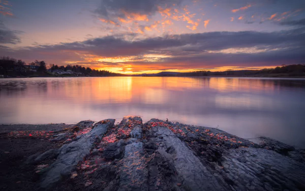 HD desktop wallpaper: serene lake sunset viewed from a rocky shore, vibrant sky reflected on calm water, a tranquil nature scene.