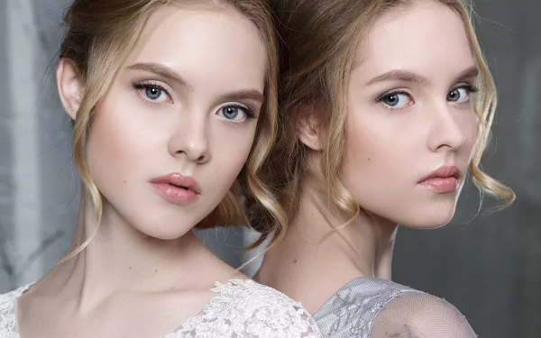 Close-up portrait of blonde twin women with light makeup, softly lit against a neutral background, used as an HD PC desktop wallpaper and background image.