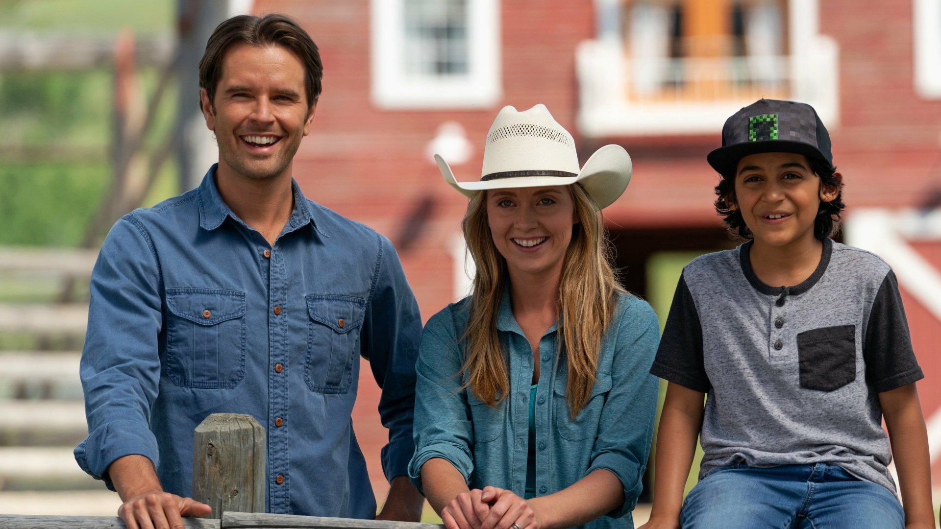 HD desktop wallpaper of three people smiling with a rural backdrop, tagged with Heartland, featuring two adults and a child in casual attire.