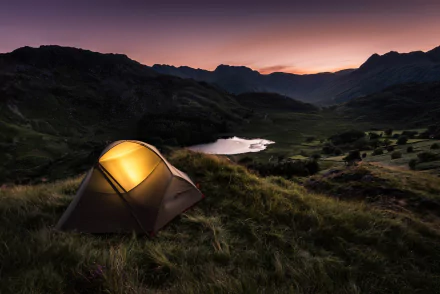 A cozy camping scene featuring a lit tent set against a stunning mountain landscape and serene lake, captured in high-definition for an inspiring desktop wallpaper.