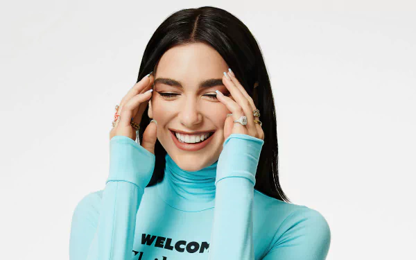 English singer Dua Lipa with black hair smiles brightly, wearing rings and a light blue turtleneck, captured in a vibrant HD desktop wallpaper.