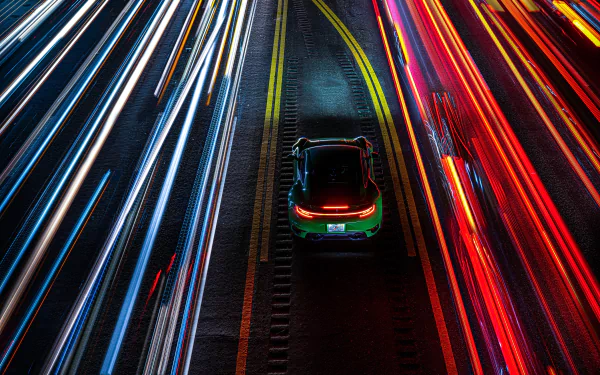 Aerial view of a green Porsche 911 Turbo threading red and blue time-lapse light trails on a highway — 8K Ultra HD PC desktop wallpaper background.