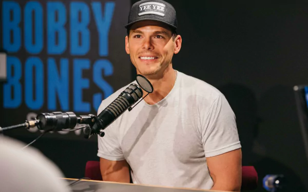 HD desktop wallpaper featuring a smiling person wearing a cap, sitting in front of a microphone with BOBBY BONES in the background.