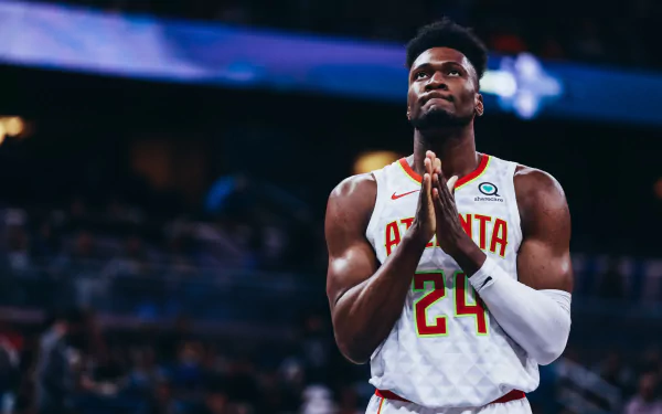 HD desktop wallpaper featuring Bruno Fernando in an Atlanta jersey with a focused expression, hands clasped together in an arena.
