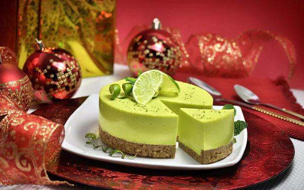 HD desktop wallpaper of a vibrant lime cheesecake with a crumb crust, garnished with lime slices, set against a festive red background with ornaments and ribbon.