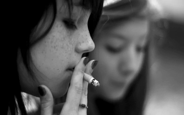 Black-and-white artistic HD wallpaper showing a close-up of a woman smoking a cigarette with smoke curling around her face and another blurred woman in the background.