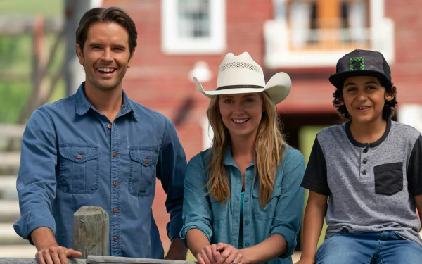 HD desktop wallpaper of three people smiling with a rural backdrop, tagged with Heartland, featuring two adults and a child in casual attire.
