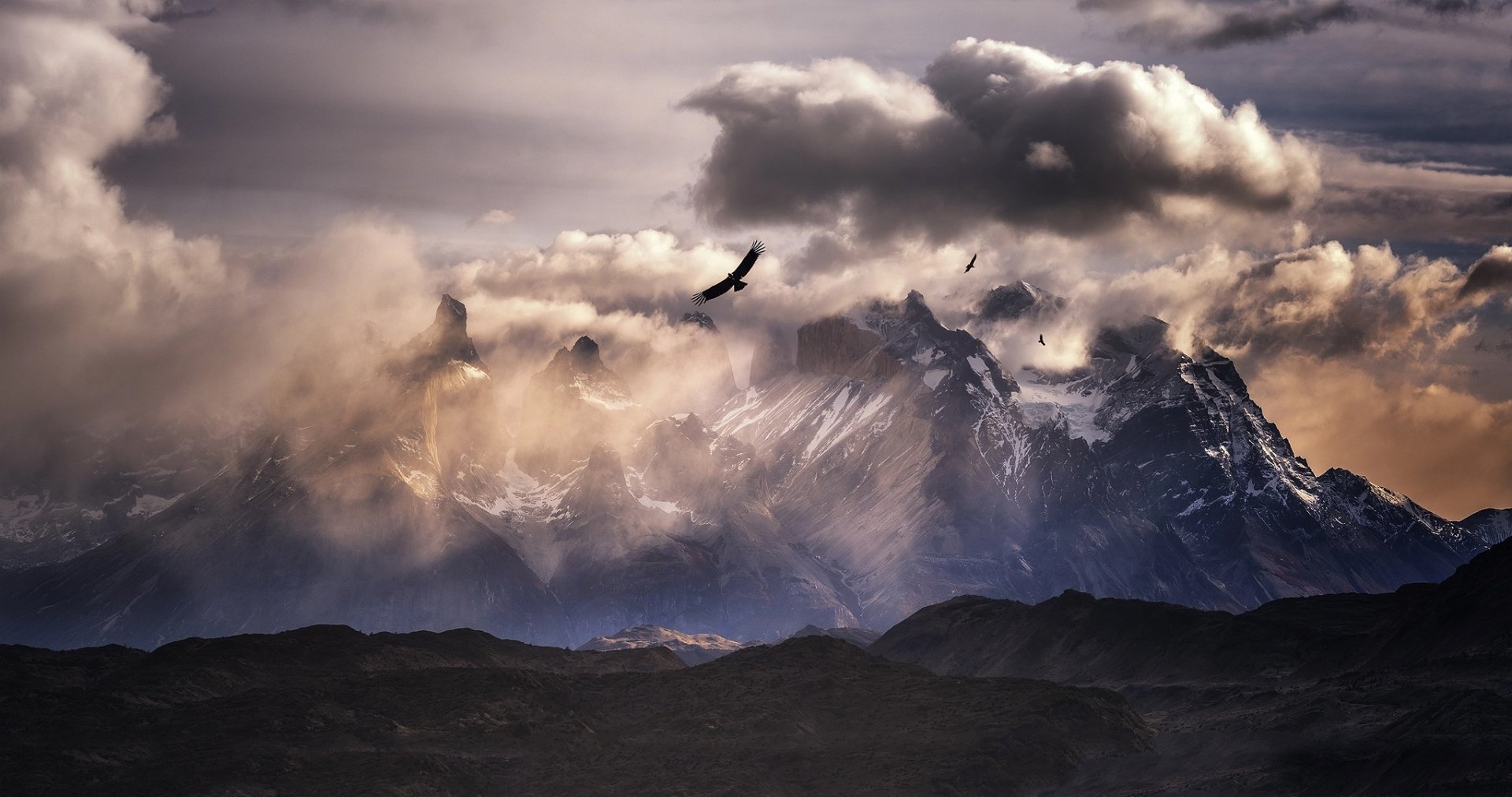 HD landscape wallpaper of the Andes mountains in South America, featuring dramatic clouds, soaring birds, and rugged natural scenery.