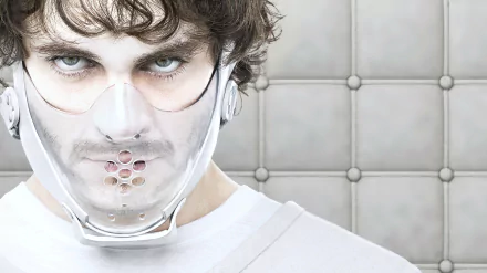 Close-up of a man wearing a restraint mask in a padded room, from the TV show Hannibal, presented as a 4K Ultra HD PC desktop wallpaper and background.