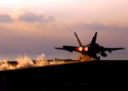 HD wallpaper showcasing a Boeing F/A-18E/F Super Hornet jet fighter taking off from an aircraft carrier at dawn, steam trailing behind.