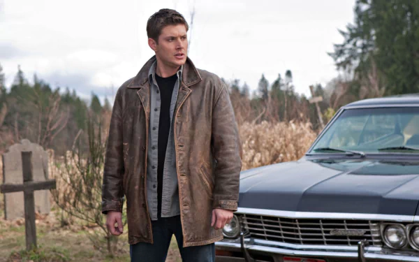 HD PC desktop wallpaper of Dean Winchester from the TV show Supernatural standing in a graveyard beside the iconic black Impala.