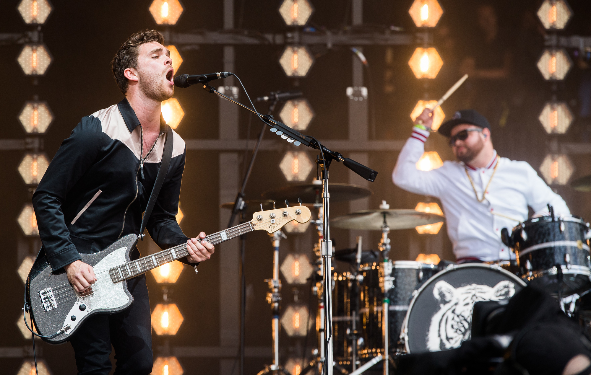 Royal Blood band members performing live on stage, guitarist singing and drummer playing in the background with dynamic lighting, perfect for HD desktop wallpaper.