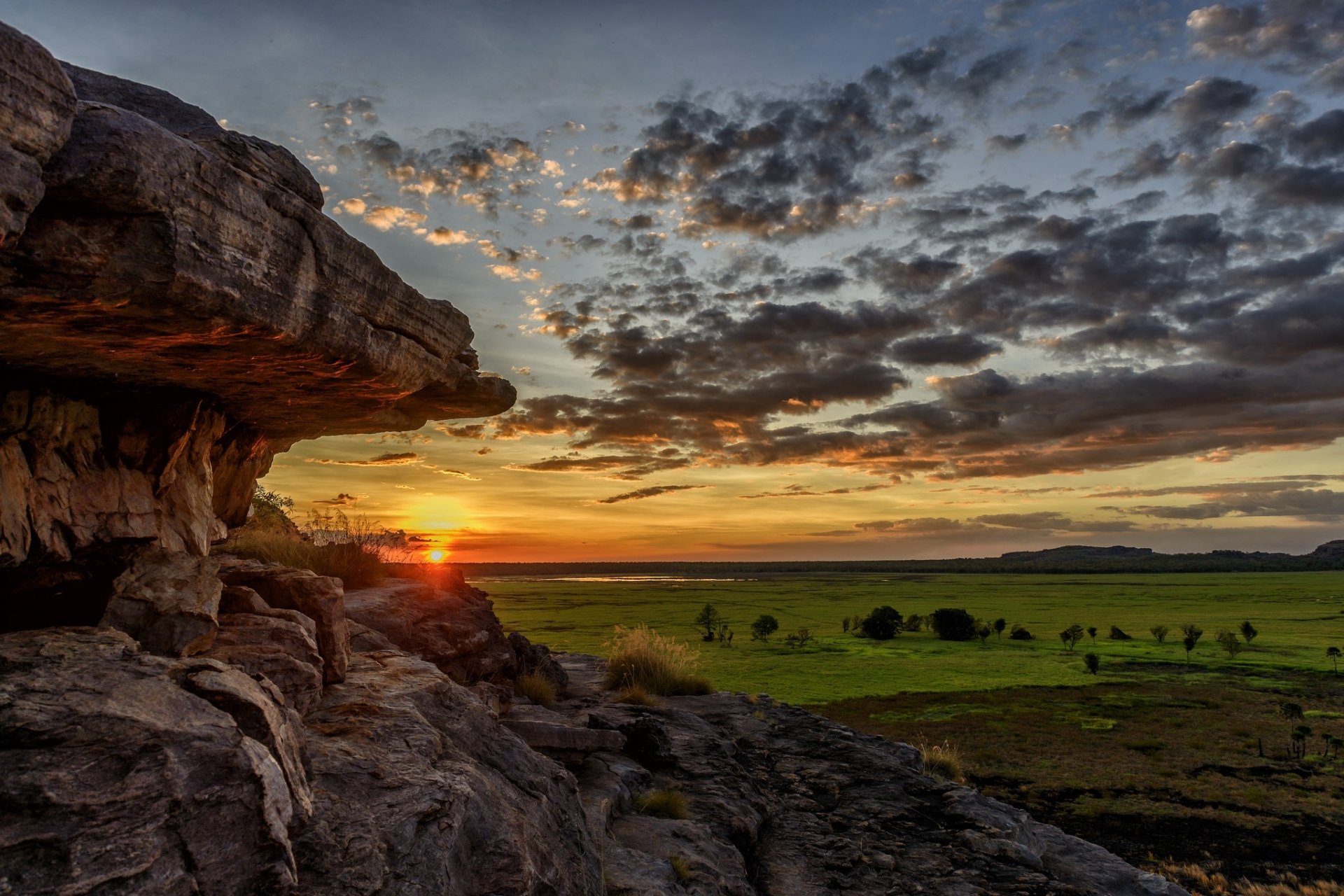 HD PC desktop wallpaper featuring a vibrant sunset over a vast green landscape with rocky cliffs and dramatic cloud formations in nature.