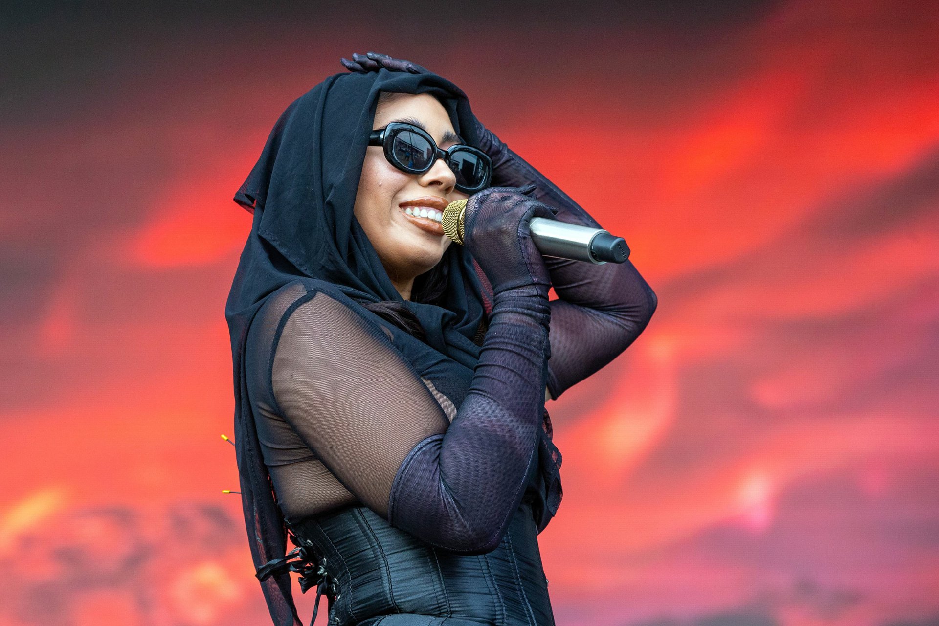 HD desktop wallpaper of a smiling performer in sunglasses holding a microphone, with a red-stage backdrop.