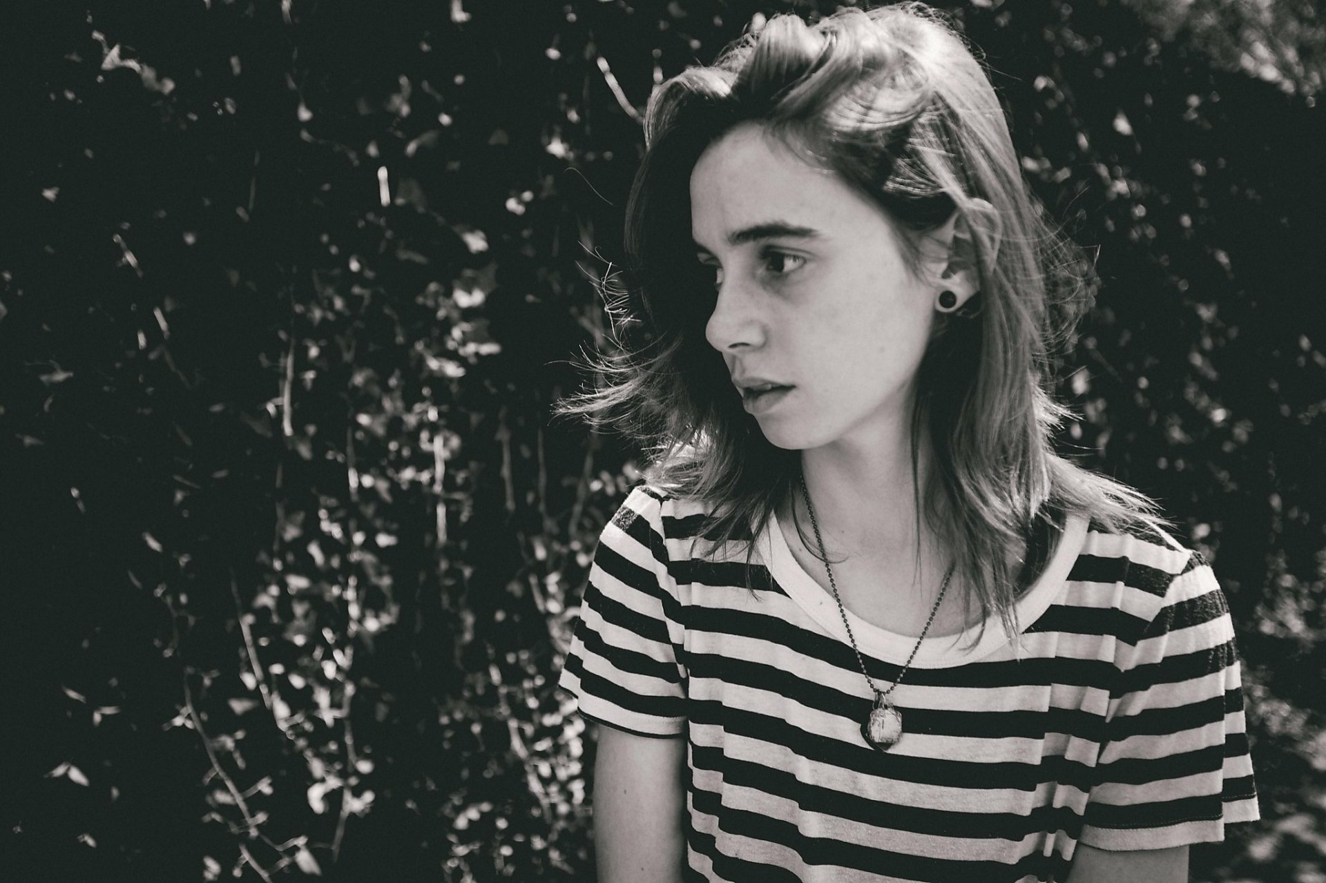 HD wallpaper featuring a black and white photo of a person with a contemplative expression, wearing a striped shirt against a leafy background.