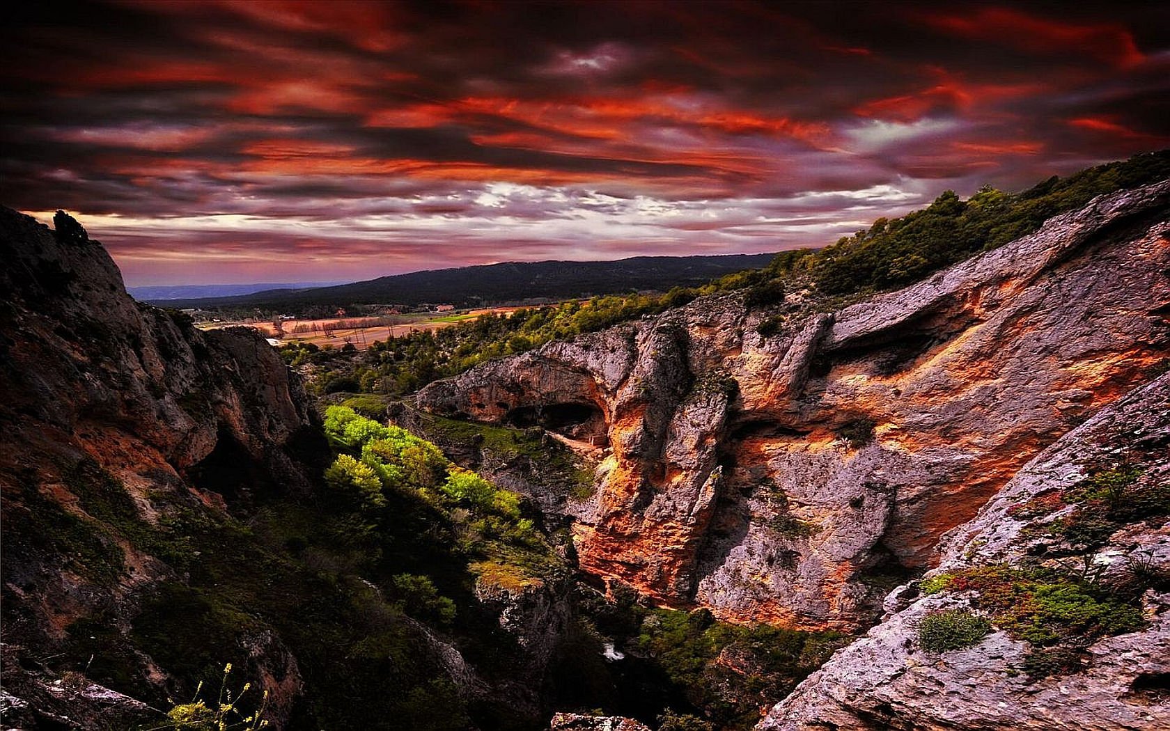 HD wallpaper of a dramatic sunset over a rugged, rocky landscape with lush greenery, blending natural beauty and vibrant colors as a striking background image.