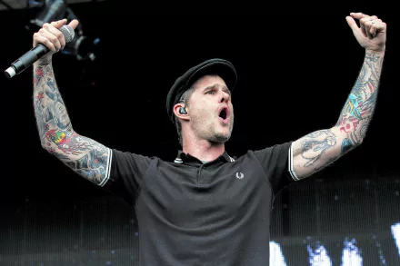 HD wallpaper of a Dropkick Murphys band member singing passionately on stage, with raised fists and tattooed arms.