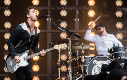 A dynamic performance by Royal Blood, showcasing the band’s energetic style, with a bassist singing passionately and a drummer intensively playing in a vibrant stage setting.