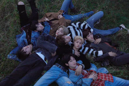 A high-definition desktop wallpaper featuring the members of ENHYPEN, lying together on grass in casual attire, creating a relaxed and youthful atmosphere.