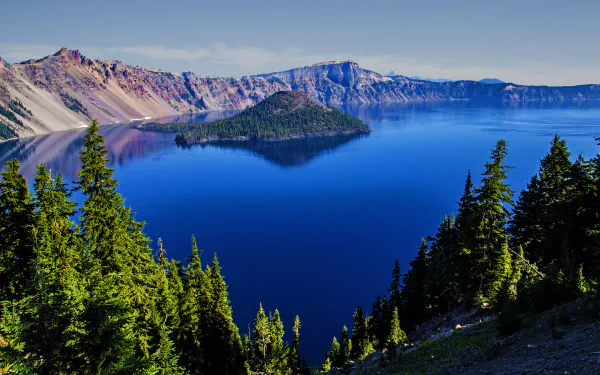 A stunning 4K Ultra HD view of Crater Lake in the USA, featuring a serene island surrounded by deep blue water and lush green forests.