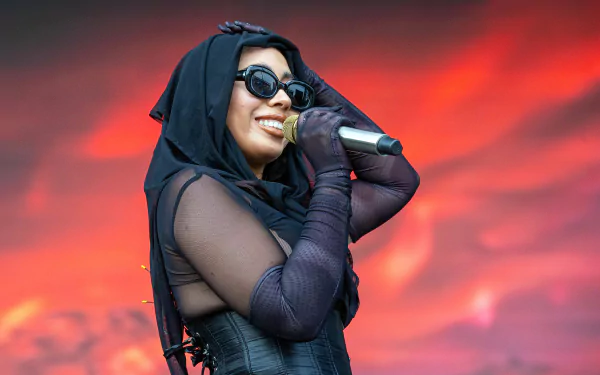 HD desktop wallpaper of a smiling performer in sunglasses holding a microphone, with a red-stage backdrop.