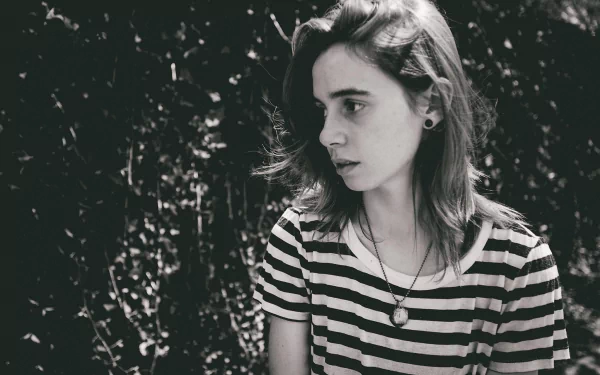 HD wallpaper featuring a black and white photo of a person with a contemplative expression, wearing a striped shirt against a leafy background.